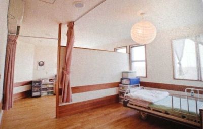 木製の仕切りと医療用ベッドがある介護施設の居室。明るく清潔な空間。